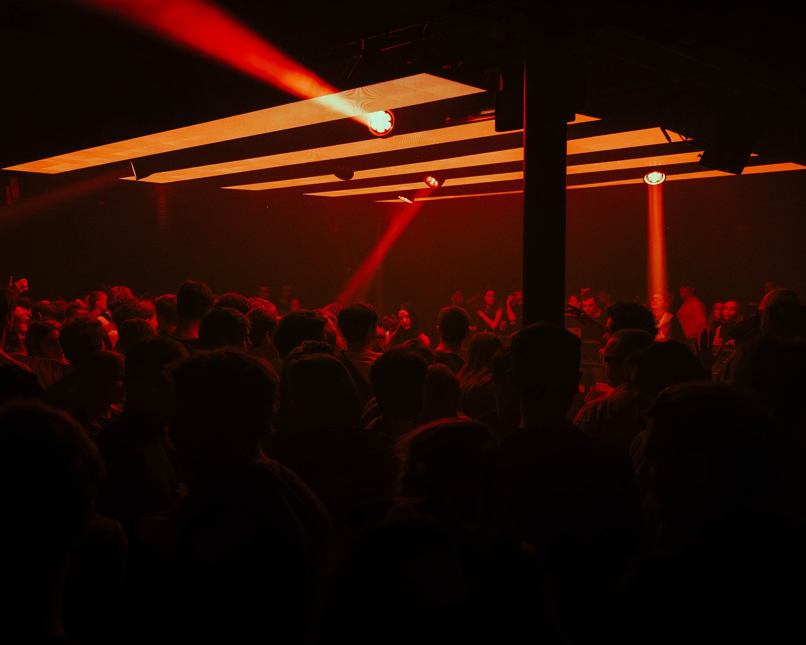 Crowd packed under crossing red and gold light beams at a KompaanEvents night